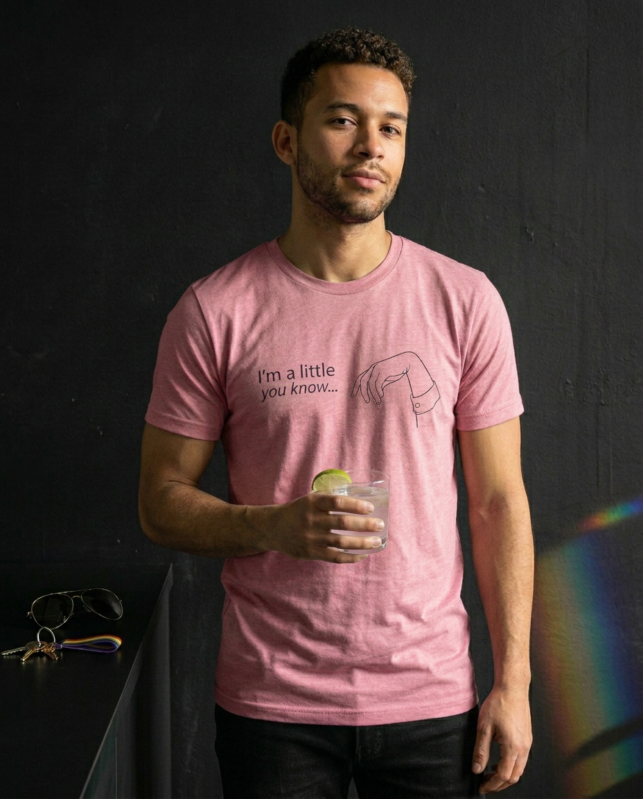 Man wearing a pink t-shirt with text and graphic, holding a glass against a dark background. X Collection: Limp Wrist Tri-Blend Graphic Tee. Funny gay shirts, funny pride shirts, pride t-shirts by Pride Clothing Co. 
