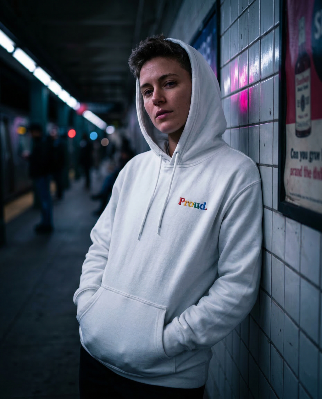 Person wearing a white hoodie with 'Proud' text in a subway setting. Proud Premium Pullover Hoodie
